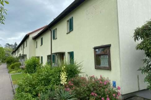 FHG am Hörnli, Reihenhaus mit hellgrüner Fassade, grünen Fensterläden und einem Vorgarten mit verschiedenen Pflanzen und Sträuchern.